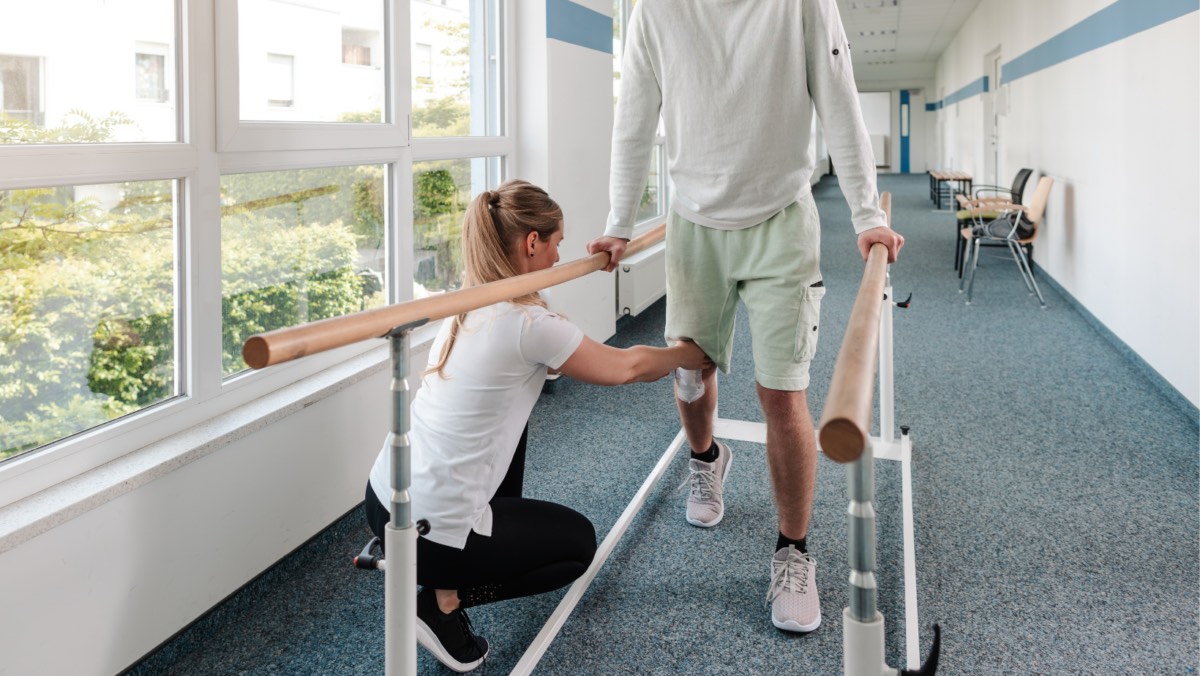 A physical therapist providing manual support to a patient practicing proper gait and walking mechanics during early-stage ACL recovery.