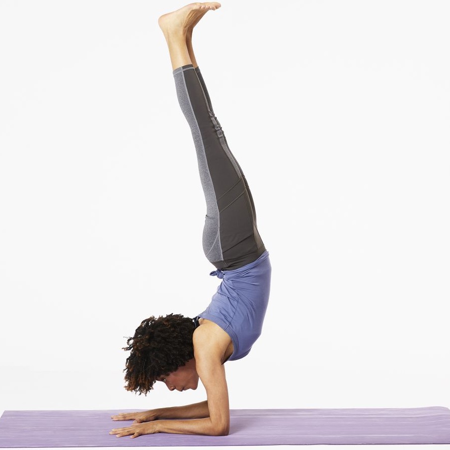Full photograph of a practitioner demonstrating a balanced elbow stand pose on forearms showing how body weight shifts safely to the arms to offload the cervical spine