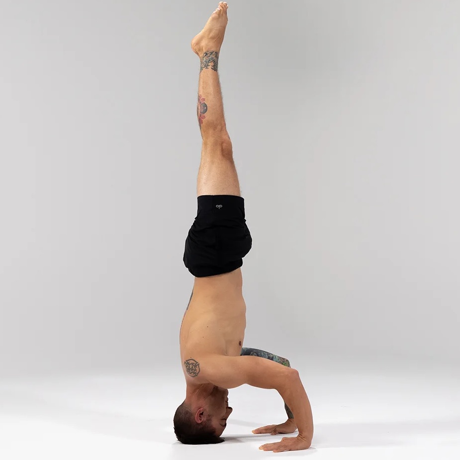 Full photograph of a yoga practitioner demonstrating a headstand pose on a mat highlighting the extreme structural loading concentrated entirely on the neck and head