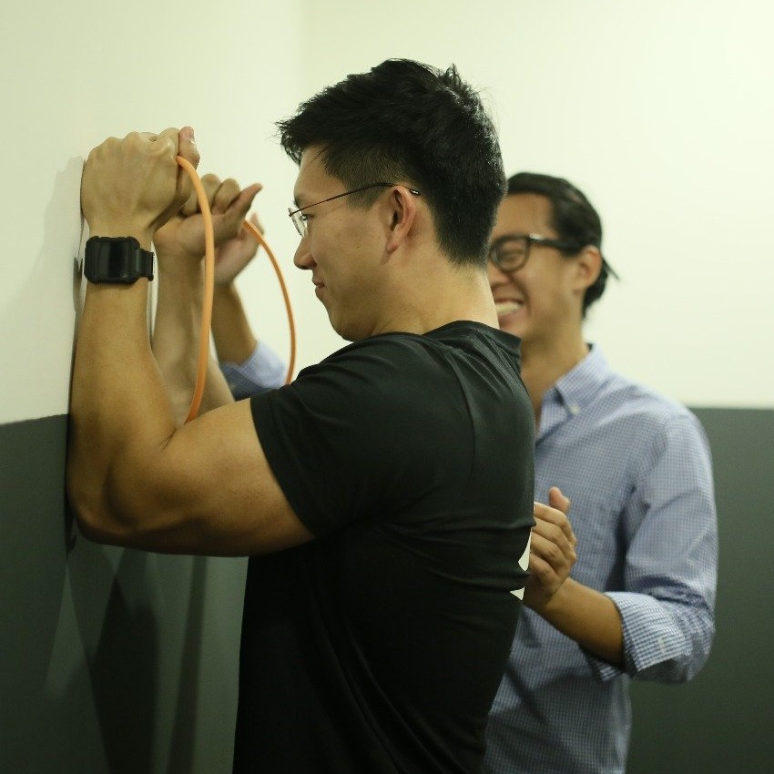 A man performing neck strengthening exercises with a resistance band to demonstrate the transition from clinical equipment to home-based active recovery.