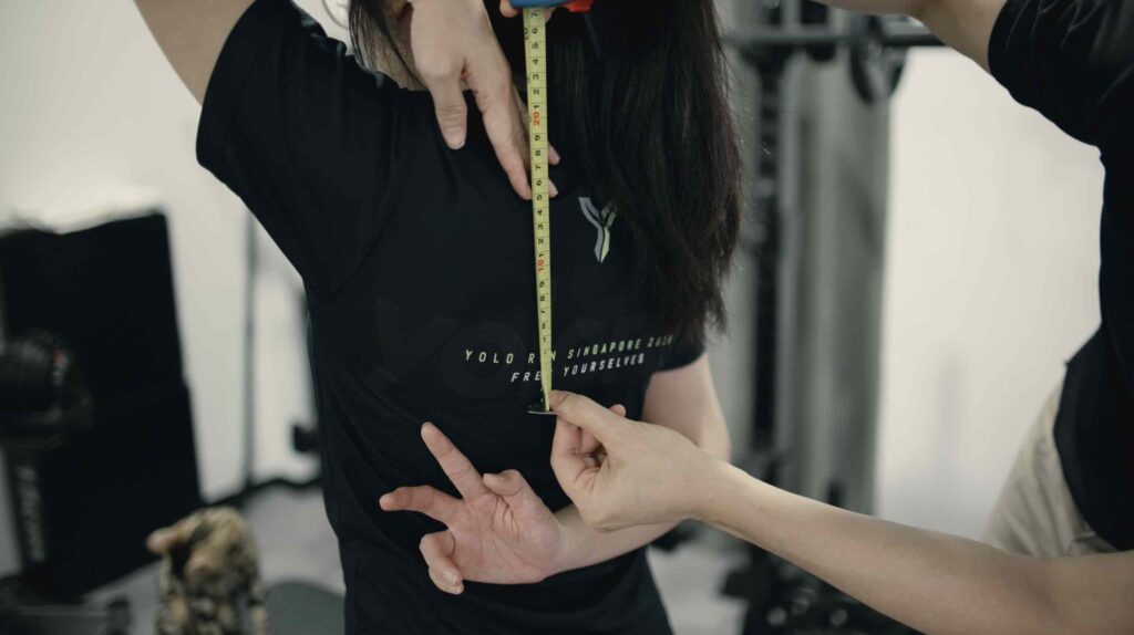Female client performing Apley’s scratch test during a shoulder mobility assessment with Chiropractor Jesse Cai.
