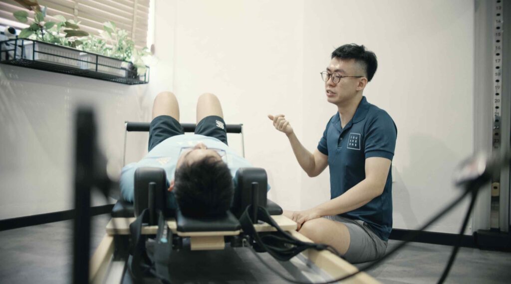 Chiropractor Jesse Cai explaining core stability techniques to a client performing an exercise on a reformer at Square One Active Recovery.