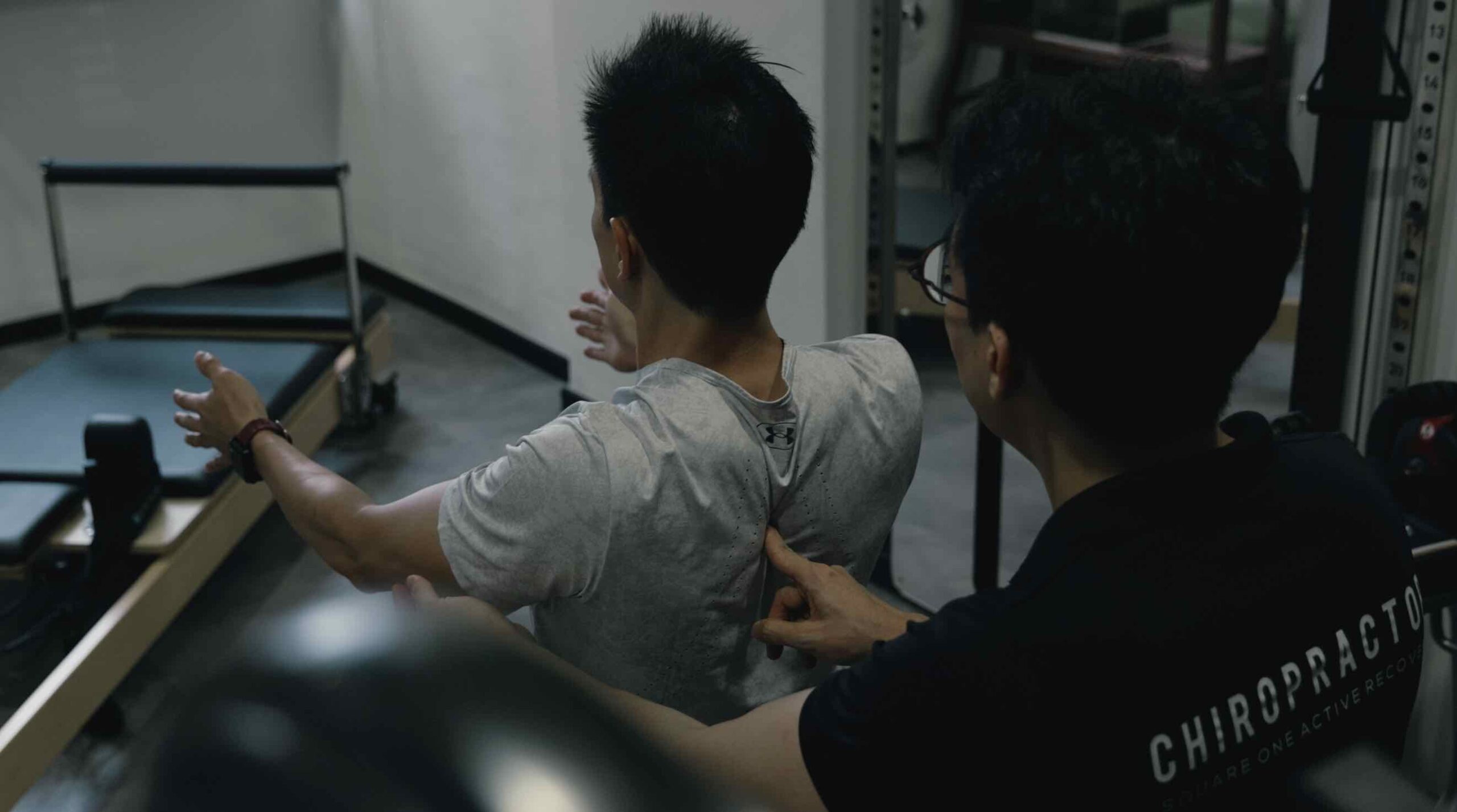 Chiropractor Jesse Cai coaching a client on scapular retraction and motor control during arm movement for neck rehabilitation at Square One Active Recovery.