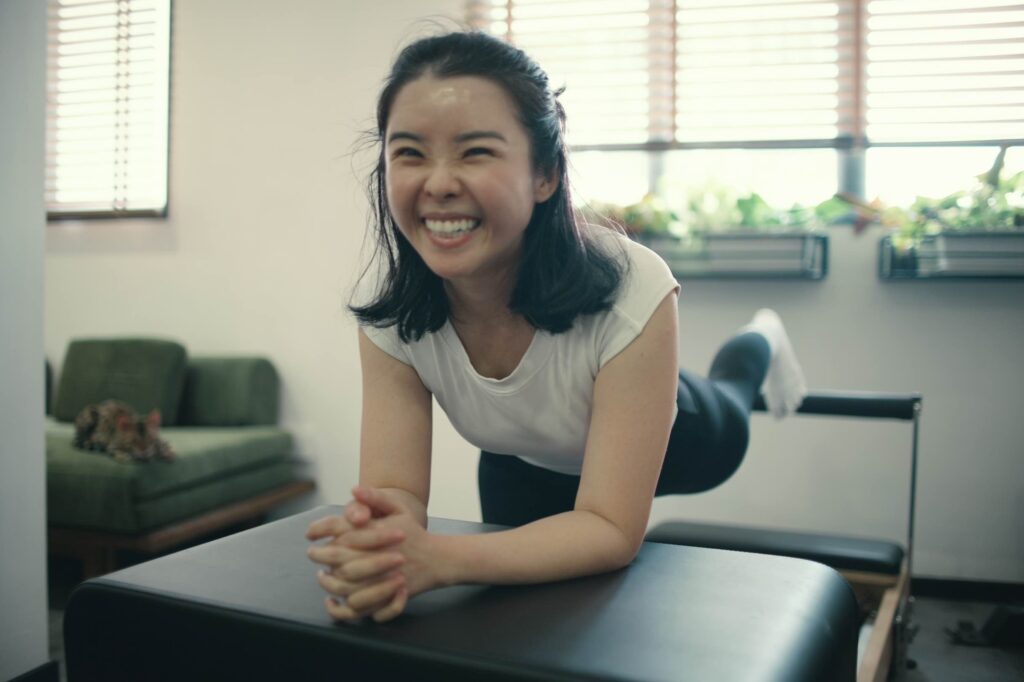 Happy woman practicing reformer Pilates at a Singapore studio to build core strength and manage lower back pain.