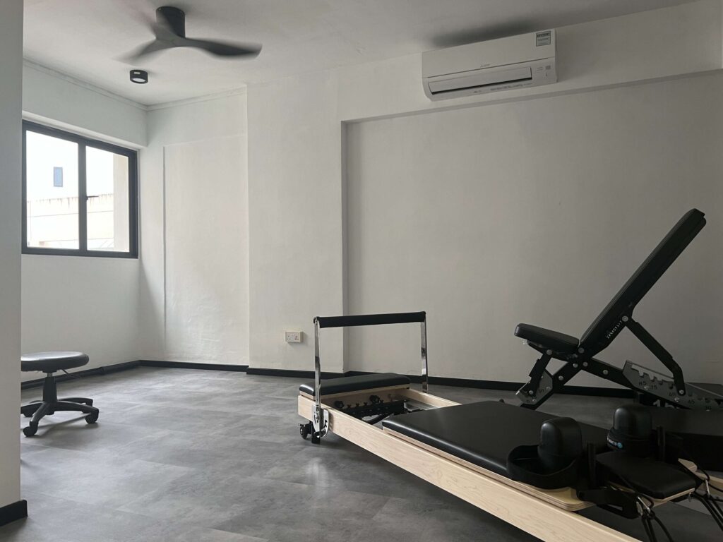 A sleek Pilates reformer machine set up inside a modern, bright HDB flat living room in Singapore.