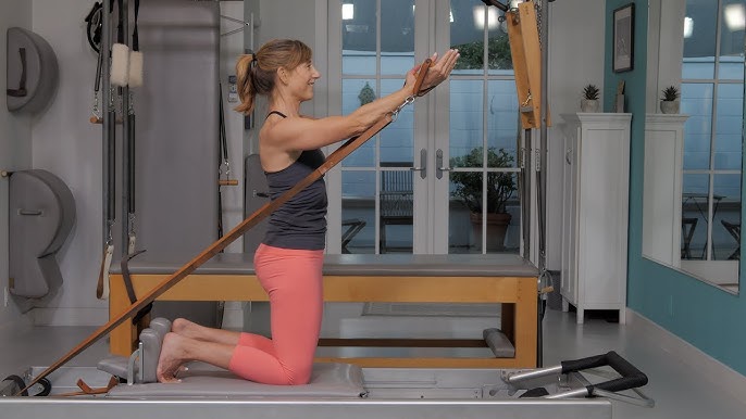 Woman performing high kneeling Pilates reformer arm circles for shoulder rehab and core stability in Singapore.