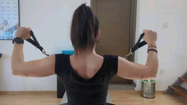 Person performing a standing resistance band pec fly in a strict horizontal plane for front delt fixator endurance.