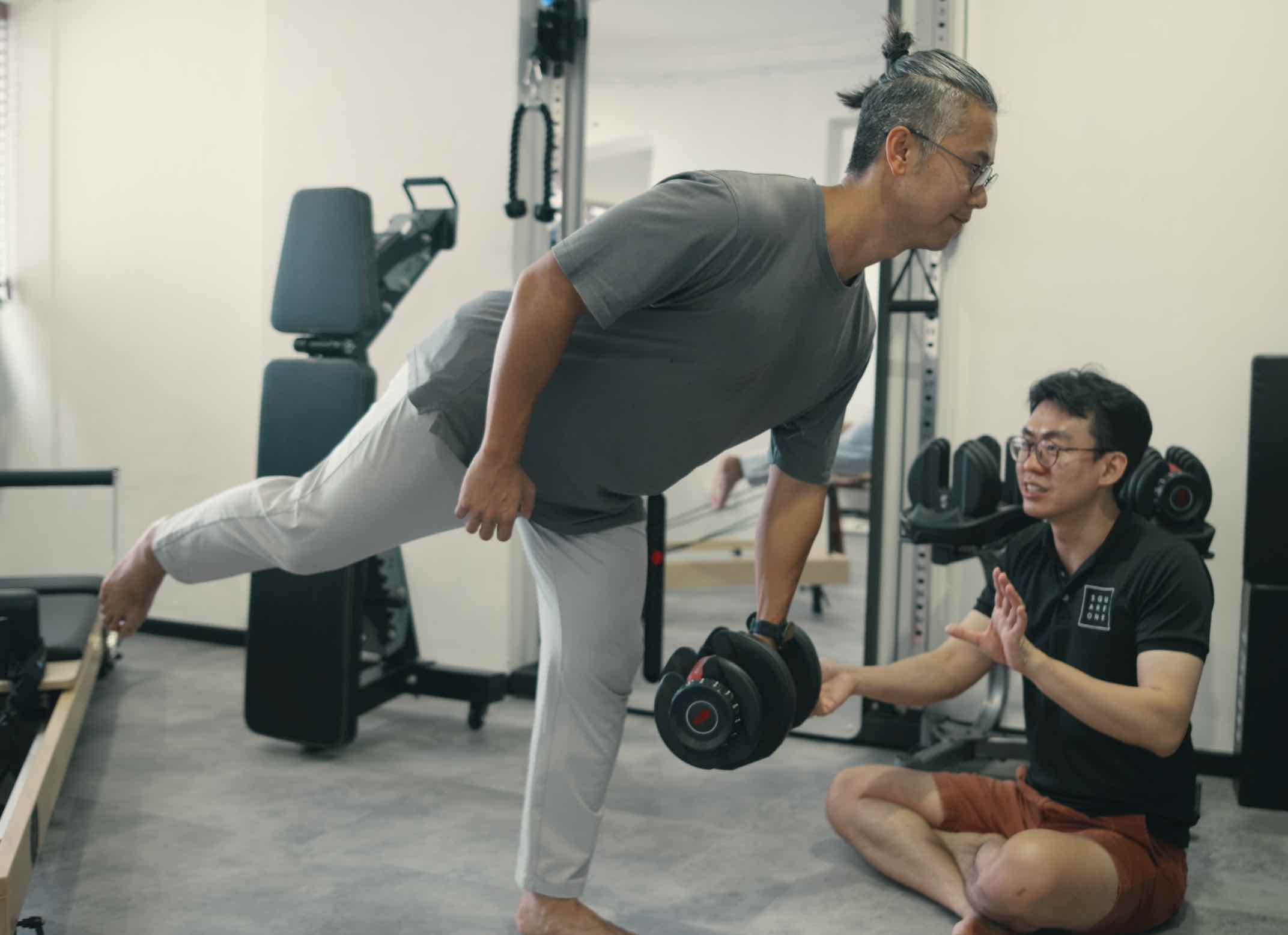 Chiropractor Jesse Cai guiding a client through a single-leg deadlift for knee pain rehabilitation, focusing on balance, stability, and intrinsic foot strength.