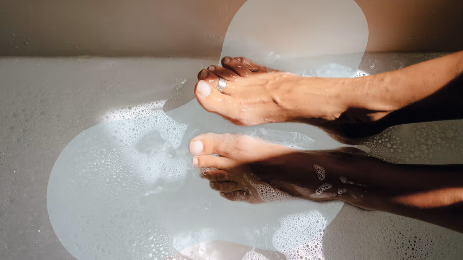 Person soaking feet in a warm water bath to promote peripheral vasodilation for acute migraine relief.